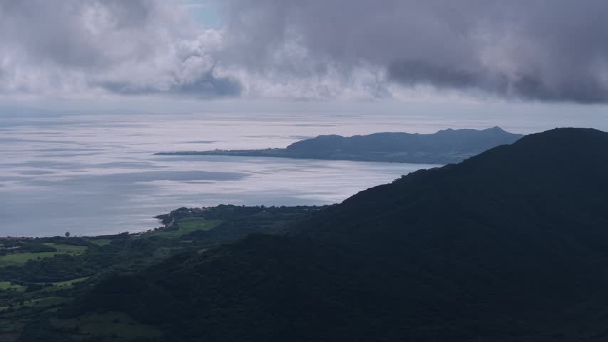 Horizontal aerial footage trucking left above Mount Omoto overlooking Torinji Town, the forested mountains and coastline of Ishigaki Island, Okinawa, Japan