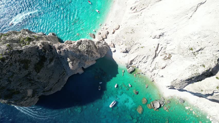 Aerial view of the iconic Navagio Beach with turquoise waters, white limestone cliffs, and small boats anchored in the bay in Zakinthos, Greece.
