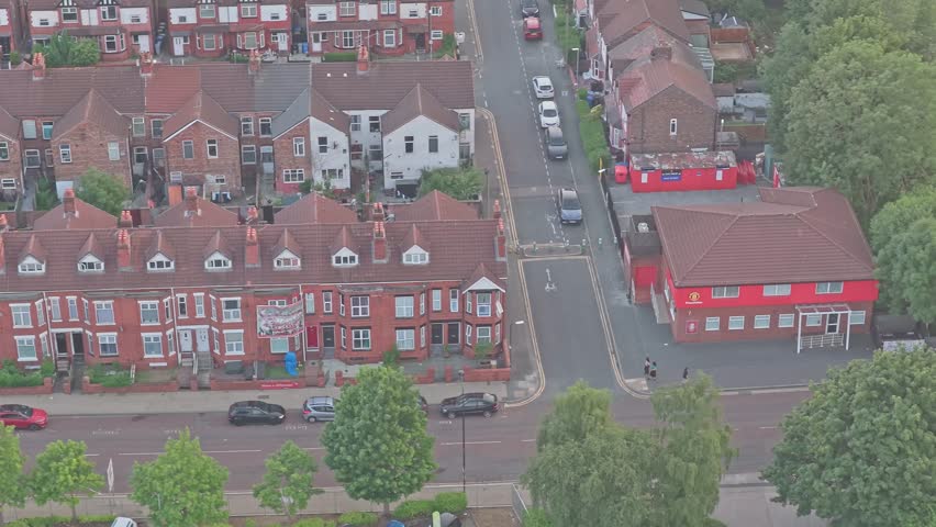 Victorian terraced houses near Old Trafford, Manchester, England, United Kingdom, revealing residential streets, local shops, parked cars and brick housing, drone forward flyover descent.