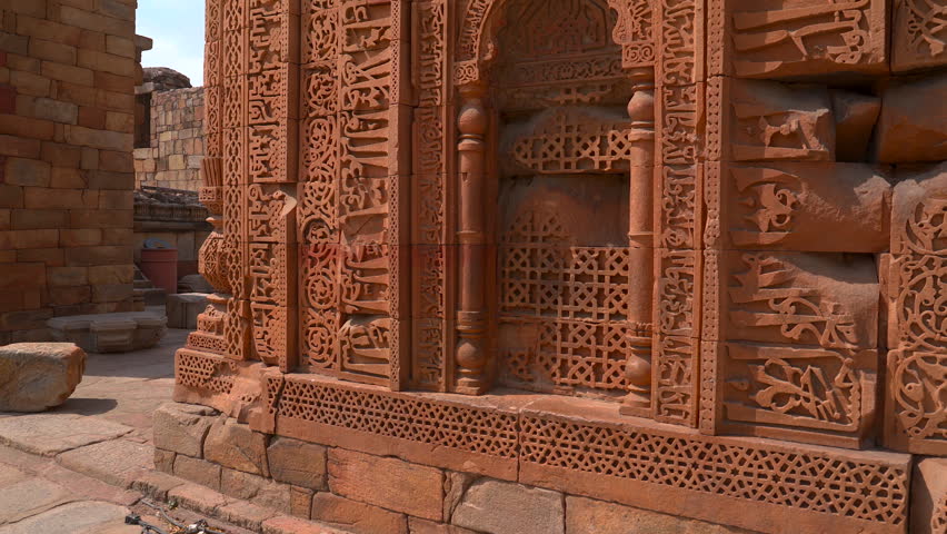 Close up shot of detailed Quranic calligraphy and geometric carvings on red sandstone walls at the Qutb Minar complex in New Delhi, India.