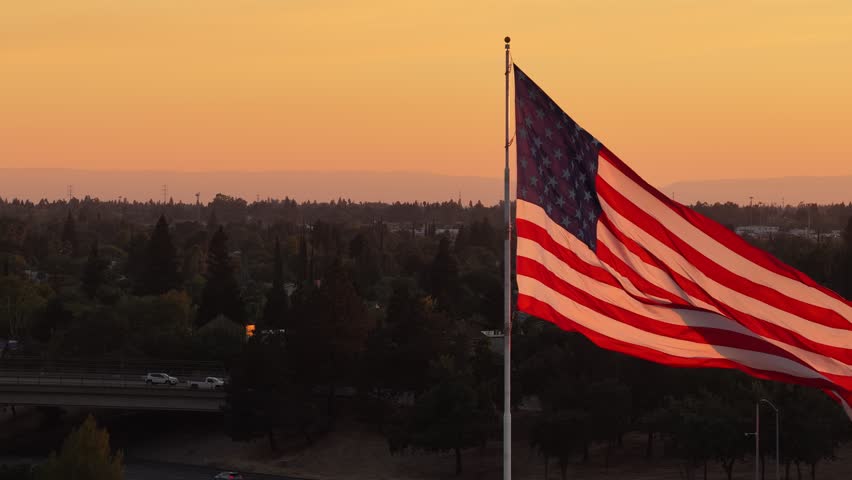 American Flag Waving On Flagpole Above Trees At Sunset