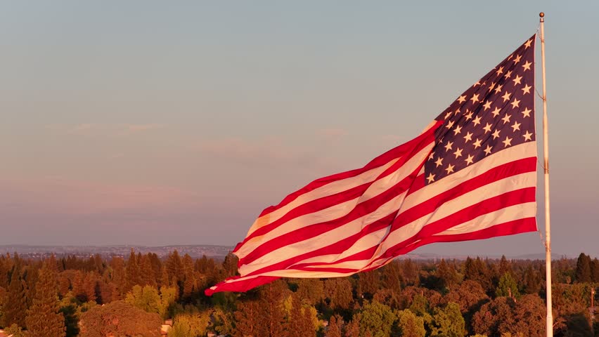 American Flag Waving On Flagpole Above Tree Canopy At Sunset
