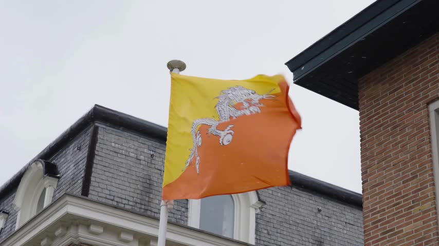 Bhutan flag waving on a pole next to a brick building