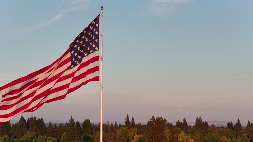 American Flag Waving On Flagpole Above Tree Canopy At Sunset