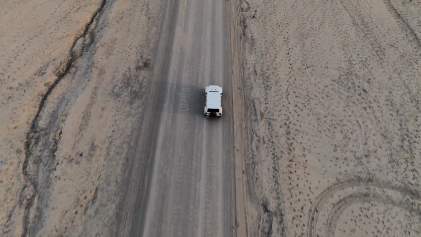 Aerial view of a white off-road vehicle driving on a dirt road near Factory Butte in a desert landscape in Wayne County, Utah, United States.