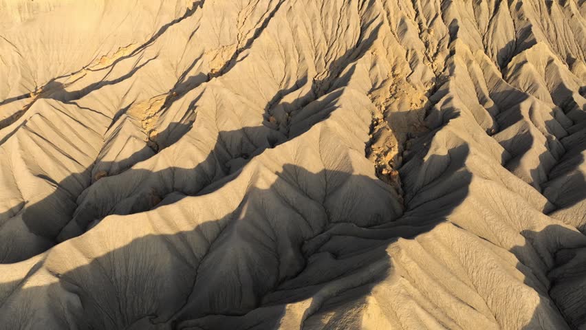 Aerial view of the rugged, eroded badlands of Factory Butte with deep ridges and shadows in the desert landscape in Wayne County, Utah, United States.