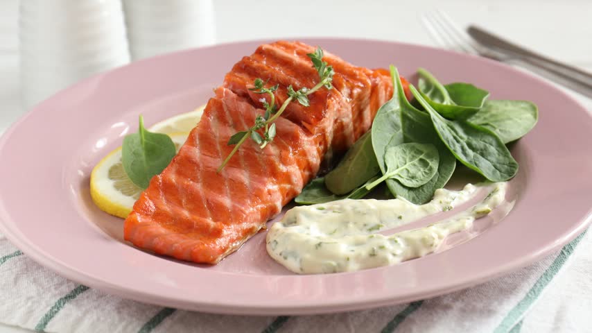 Woman squeezing lemon juice onto piece of grilled salmon at table, closeup