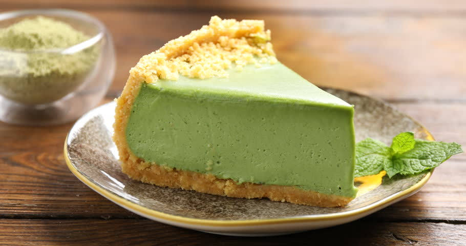 Woman putting cup of tea and piece of tasty matcha cheesecake at wooden table, closeup