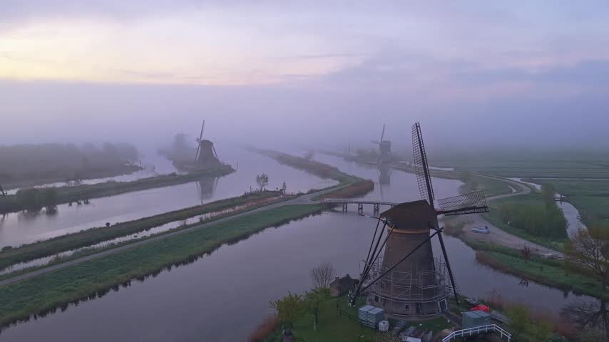 Majestic aerial view of the iconic windmills at kinderdijk, netherlands during a foggy sunrise. The historic structures reflect in calm canals