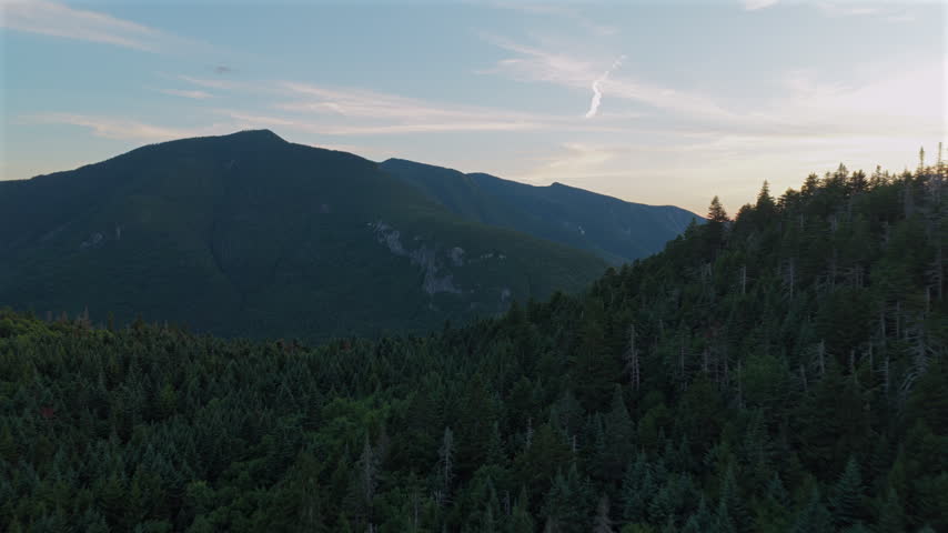 Forward moving aerial view pushes over an evergreen ridge, revealing the expansive forest covered Sandwich Range near the Pemigewasset Overlook in New Hampshire