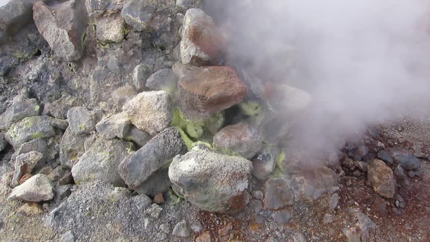 Aerial drone view of a steaming sulfur vent at Namafjall Hverir geothermal field near Lake Myvatn in North Iceland featuring mineral stained rocks rising steam and volcanic ground.