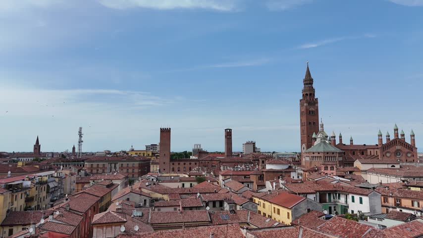 Cremona historic center shows the Torrazzo, Cathedral and Baptistery above dense terracotta rooftops in Lombardy, Italy, with medieval brick towers and church spires across the skyline, lateral pan.