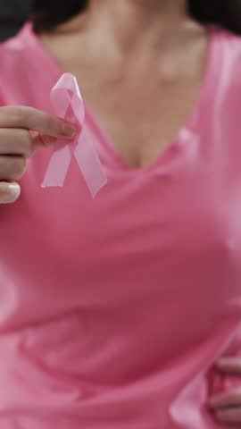 Ribbon over a anchor icon over mid section of woman holding a pink ribbon against black background. breast cancer awareness concept