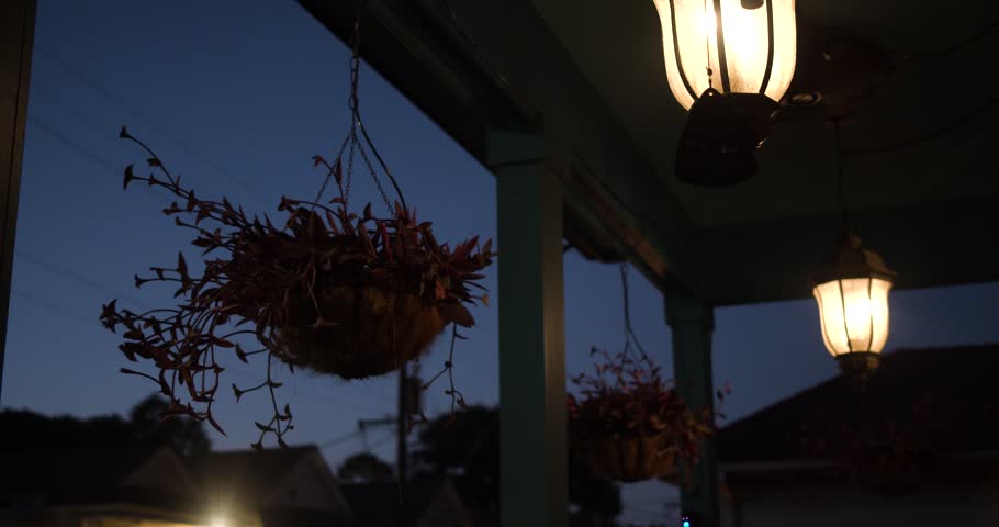 Warm porch lanterns glow against the blue evening sky in New Orleans. Hanging plants and classic Southern architecture create a peaceful cinematic residential scene.