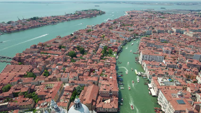 High angle aerial view over historic architecture, red rooftops, and boat traffic along the Grand Canal in Venice, Italy.