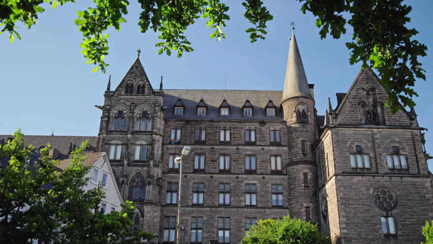 Neo-Gothic Old University (Alte Universitat) of Philipps-Universitat Marburg, framed by summer foliage in Marburg, Germany.