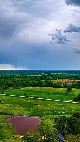 Storm clouds above farmland with pond and rolling countryside, aerial hyperlapse towards rainstorm