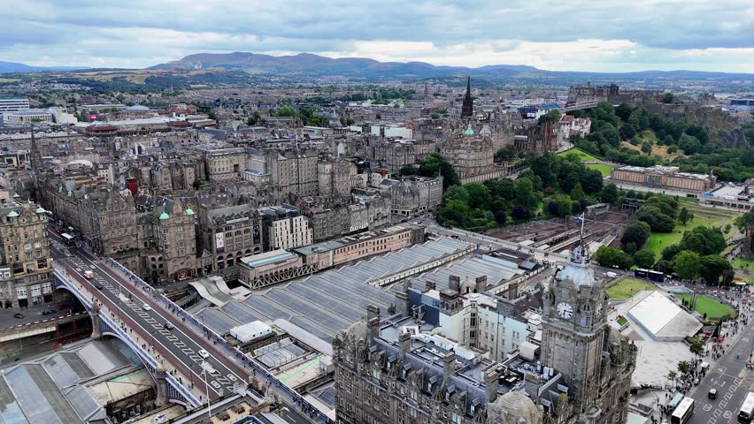 Aerial flyover of Edinburgh Waverley railway station amid historic architecture. Scotland.