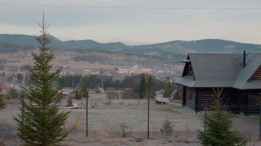 Morning light fills the mountain landscape as trees and houses come into view. The scene captures the quiet start of a new day in the mountains.