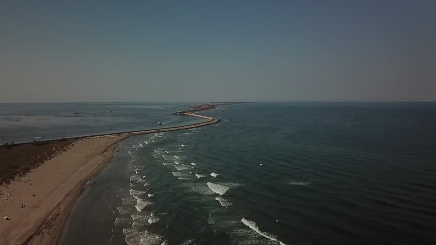 Aerial view of the outer Venice Lagoon near Pellestrina, with a narrow sandbar and coastal road dividing calm lagoon waters from the Adriatic Sea waves.