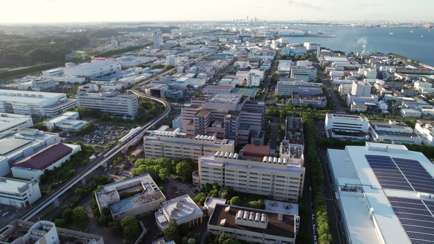 Wide aerial drone view over the Fukuura industrial district in Yokohama, Kanagawa, Japan. Factories, commercial buildings, the elevated Kanazawa Seaside Line and the waterfront are visible.