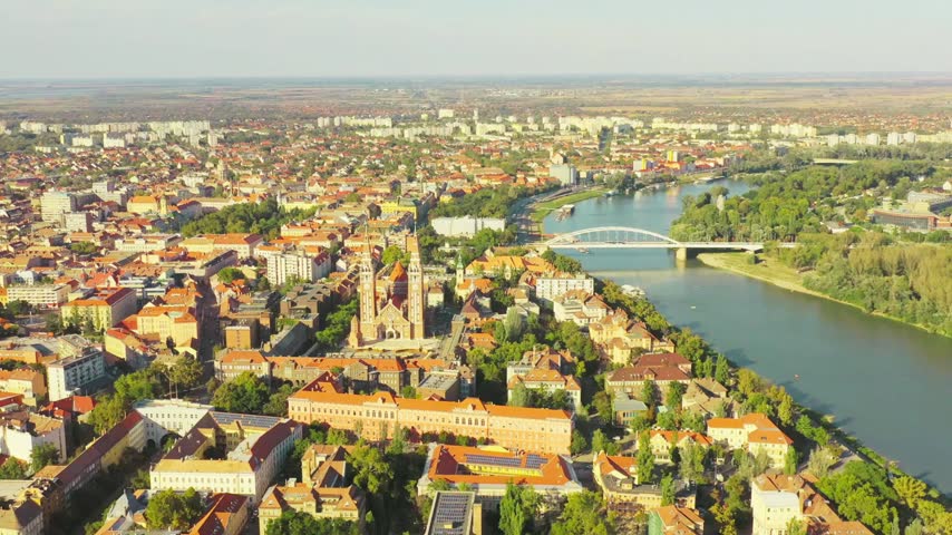 Szeged, Hungary unfolds from above as aerial footage reveals the cityscape, historic architecture, streets, rooftops, green spaces, and surrounding urban landscape. The elevated perspective captures the distinctive character and cultural heritage of this Hungarian city.