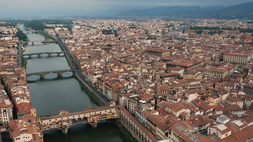 High-angle aerial drone shot panning across the historic cityscape of Florence, revealing iconic landmarks including Ponte Vecchio and Florence Cathedral.