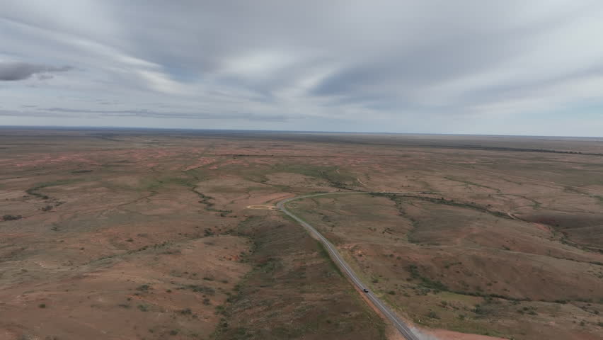 High aerial drone tracking shot following a vehicle along a winding remote road through the vast outback landscape near Silverton and Broken Hill, New South Wales, Australia.