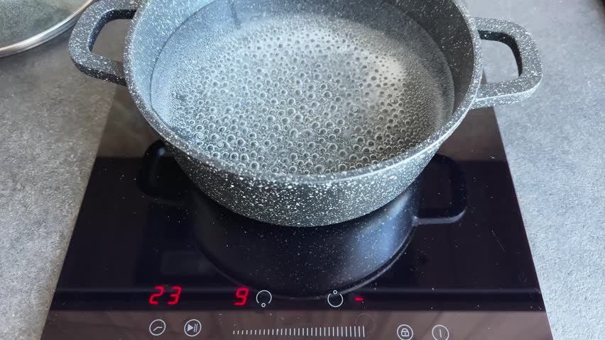 Water heating in the cast aluminum pot with granite non-stick coating on an induction cooker, view while panning
