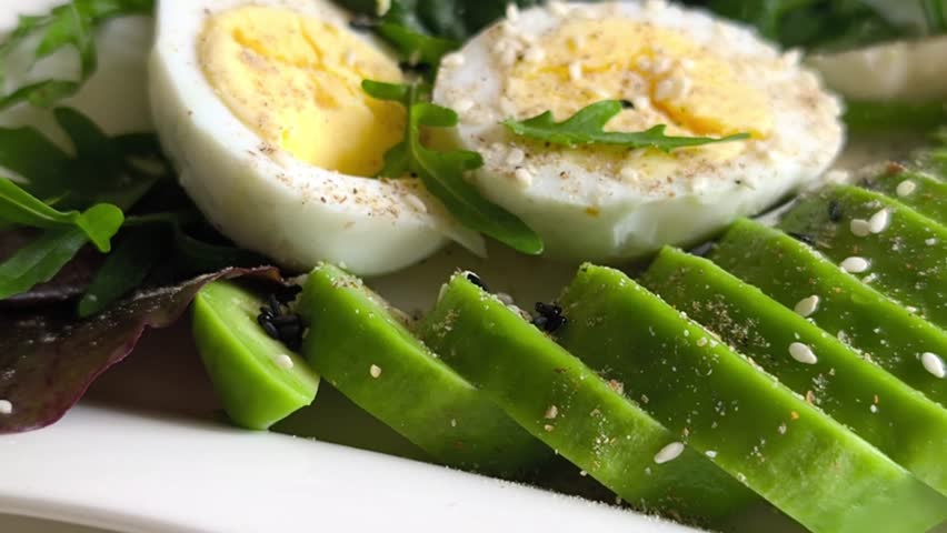 Close up of sliced egg with spices arugula and avocado. Nutritious rich meal features egg protein and pieces of fried sausage on salad base. Organic culinary for homemade keto nutrition plan.