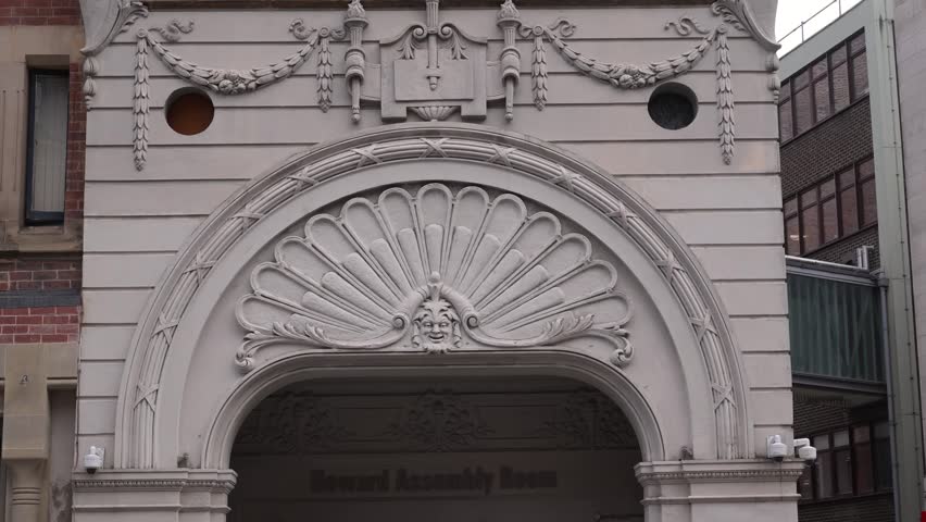Ornate Howard Assembly Room entrance arch with carved green man face and shell motif framed by neighbouring buildings.