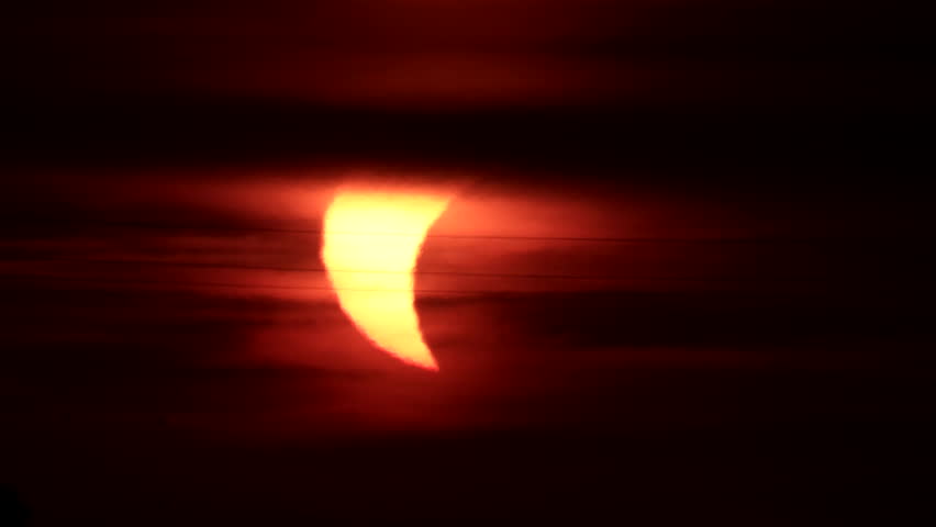 Silhouette of a commercial airplane flying across the crescent sun during a partial solar eclipse at sunset, framed by dark atmospheric clouds. Clip 03 - Sequence.