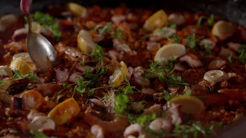Hand serving a portion from a seafood paella with prawns octopus and lemon wedges