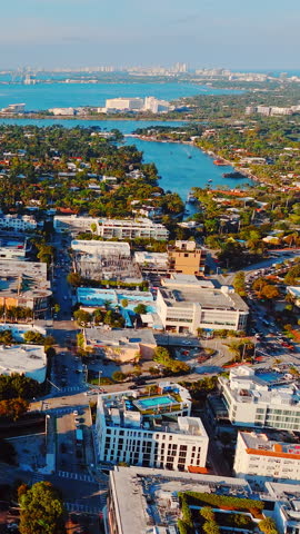 Residential neighborhood with waterway, Miami, Florida. Elevated drone view of urban street, house, tree and blue ocean inlet under clear daytime sky. Vertical video.