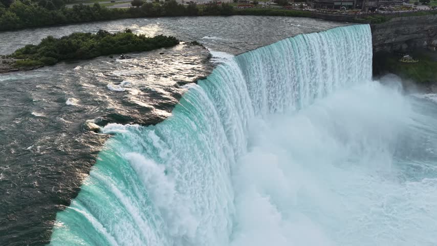 A steady, stationary aerial drone shot captures the powerful turquoise waters rushing over the brink of the Horseshoe Falls next to Terrapin Point, surrounded by rising white mist