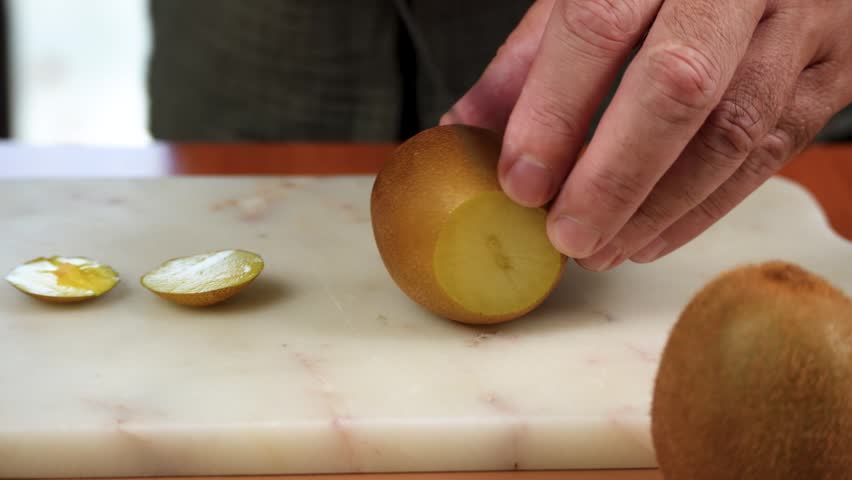 A ripe golden kiwi is cut open on a kitchen board during fruit preparation. Rotating footage highlights Actinidia chinensis with its bright yellow flesh.