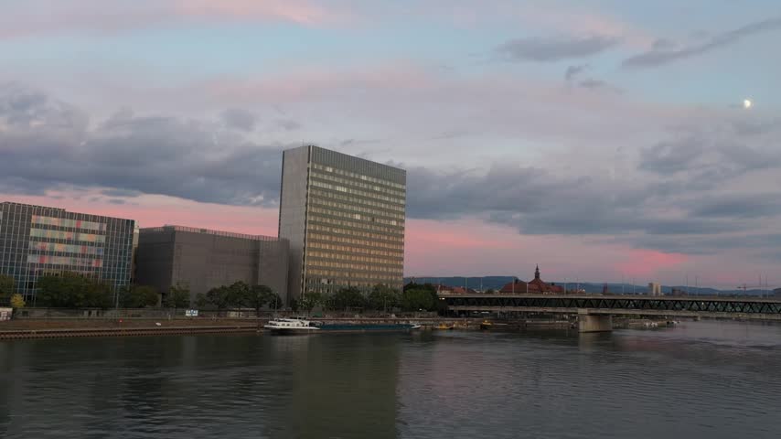 A modern urban landscape with a tall skyscraper by a river at dusk.