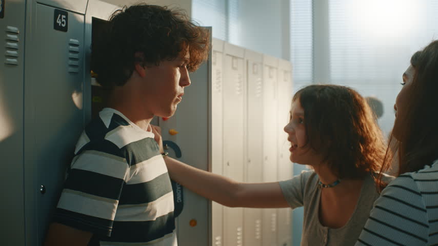 Humiliated Teenage Boy Standing by Metal Lockers While Two Female Classmates Stand Opposite, Smirking and Laughing. Psychological Abuse, Toxic Mockery, and Emotional Bullying in Modern High School.