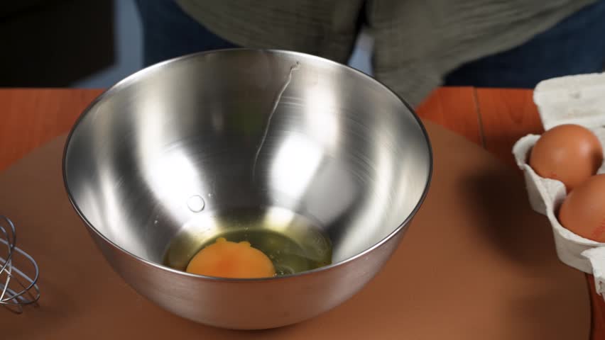 Fresh eggs are cracked into a stainless steel bowl to prepare an omelet mixture. Rotating kitchen footage captures a simple high-protein breakfast step.
