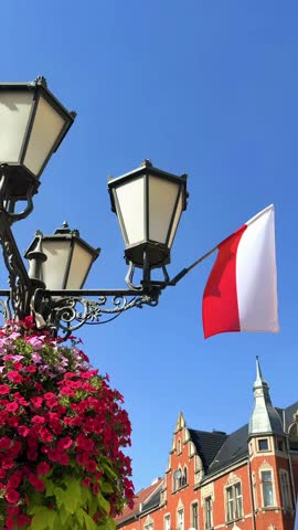 Decorative street lamp with colorful flower planters and Polish national flag on a city street, urban decoration and patriotic symbol in Poland during summer