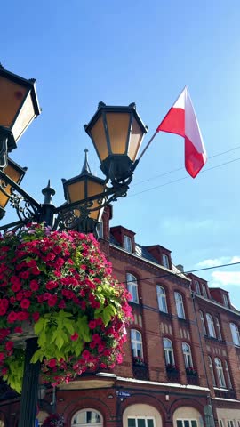 Decorative street lamp with colorful flower planters and Polish national flag on a city street, urban decoration and patriotic symbol in Poland during summer