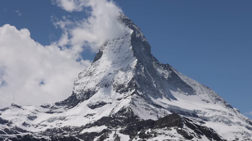 View of the iconic Matterhorn peak with snow-covered slopes and clouds drifting around the summit in Zermatt, Valais, Switzerland.