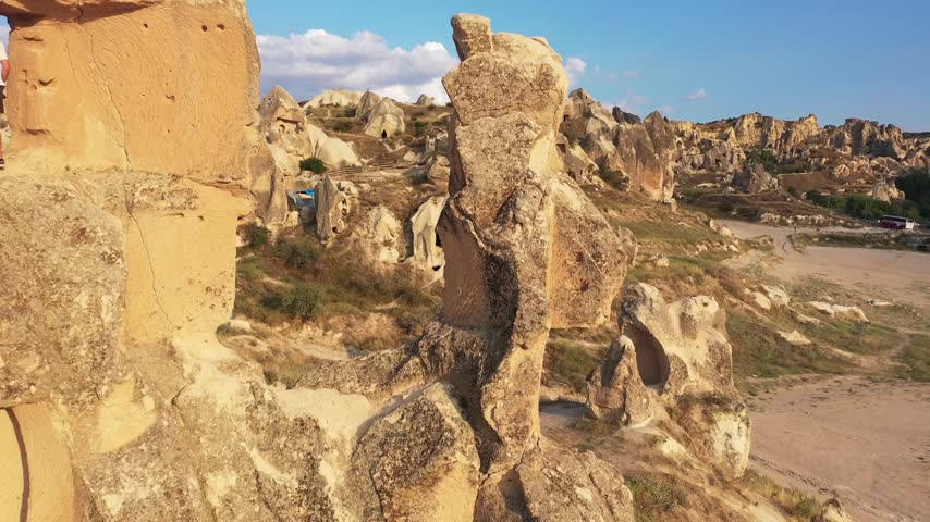 Panoramic aerial drone view of white rock formations, conical fairy chimneys, and flat-topped tuff mountains in Rose Valley, Cappadocia, Nevsehir, Turkey under a clear blue sky.
