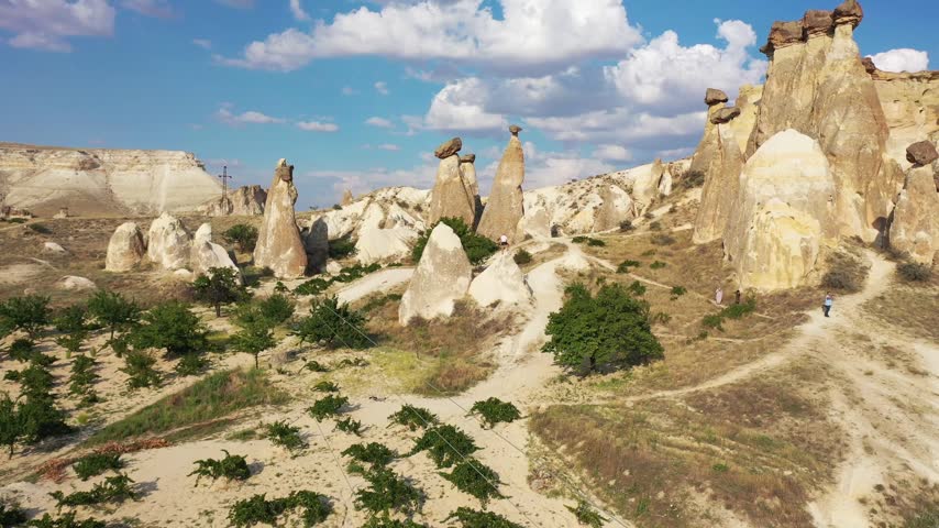 Panoramic aerial drone view of white rock formations, conical fairy chimneys, and flat-topped tuff mountains in Rose Valley, Cappadocia, Nevsehir, Turkey under a clear blue sky.