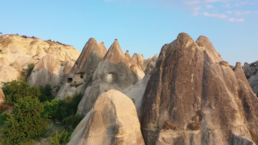 Panoramic aerial drone view of white rock formations, conical fairy chimneys, and flat-topped tuff mountains in Rose Valley, Cappadocia, Nevsehir, Turkey under a clear blue sky.