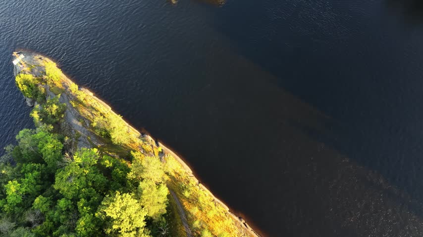 Aerial panoramic view of medieval Olavinlinna Castle surrounded by Lake Saimaa under a blue sky in Savonlinna, Finland.