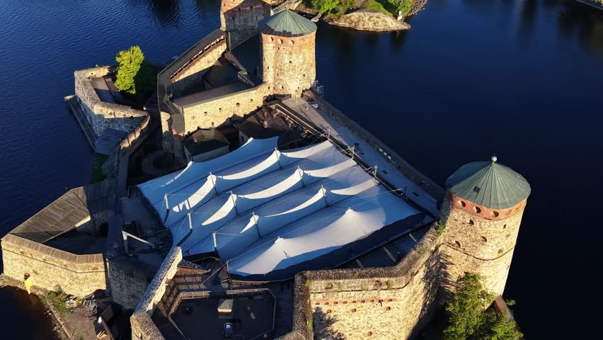 Aerial panoramic view of medieval Olavinlinna Castle surrounded by Lake Saimaa under a blue sky in Savonlinna, Finland.