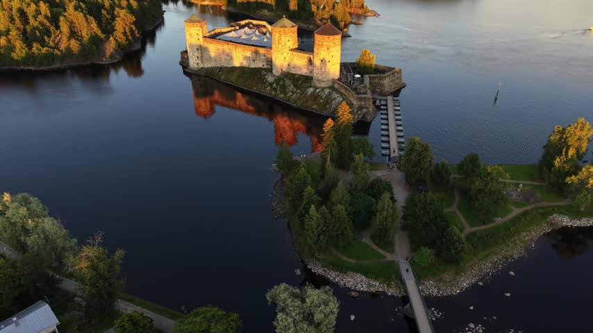 High aerial view of medieval Olavinlinna Castle illuminated by golden hour sunset light on Lake Saimaa in Savonlinna, Finland.