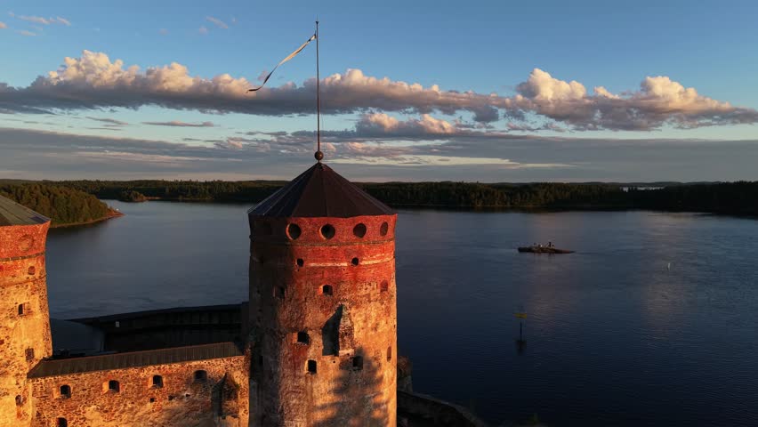 High aerial view of medieval Olavinlinna Castle illuminated by golden hour sunset light on Lake Saimaa in Savonlinna, Finland.
