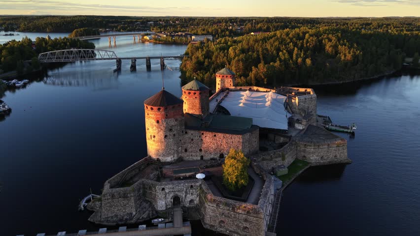 Aerial panoramic view of medieval Olavinlinna Castle surrounded by Lake Saimaa under a blue sky in Savonlinna, Finland.